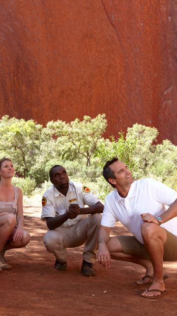 people crouching in the shadow of Ayers Rock